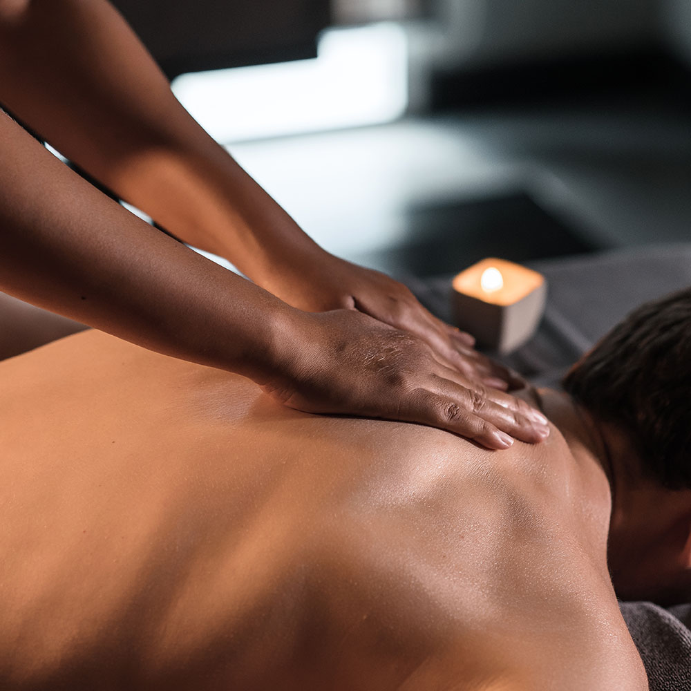 Massage therapist using Swedish Massage hand techniques to knead, man's upper back.